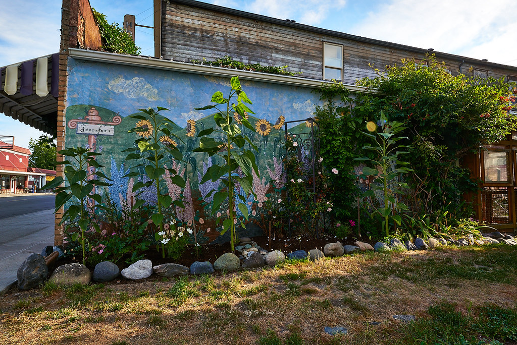 A small business storefront with a hand-painted mural and flower garden out front